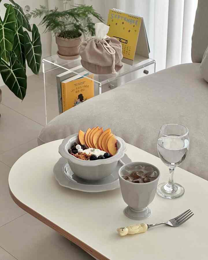 White and natural-toned living room featuring transparent acrylic side table, sofa, and brunch tableware in a cozy home cafe setup
