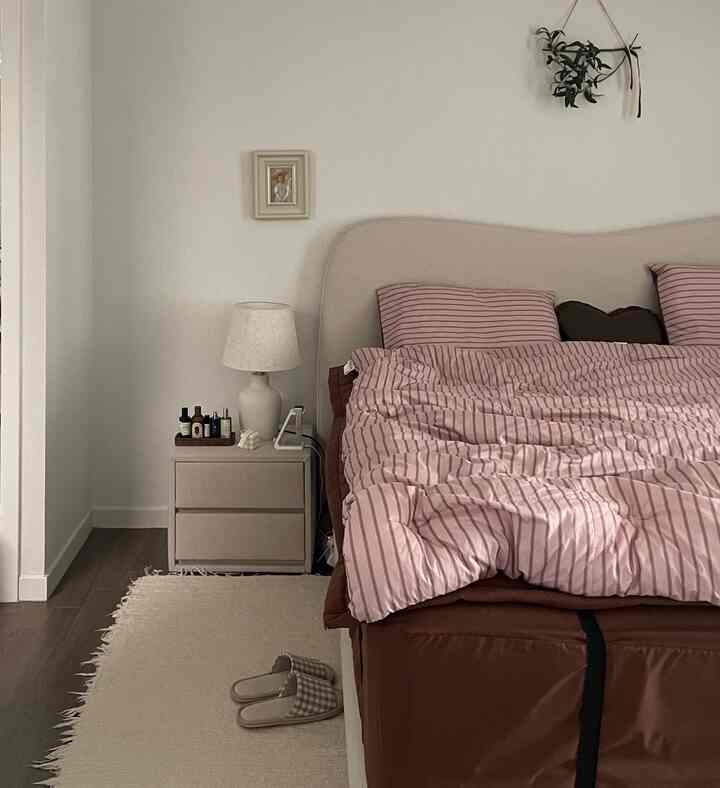 Beige-toned bedroom featuring a nightstand, pink striped bedding, and brown mattress in a simple setting