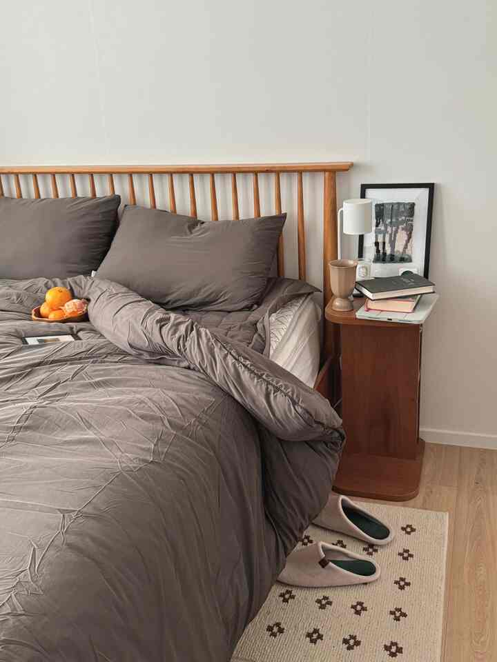A warm bedroom featuring muted gray bedding and wood-toned furniture.