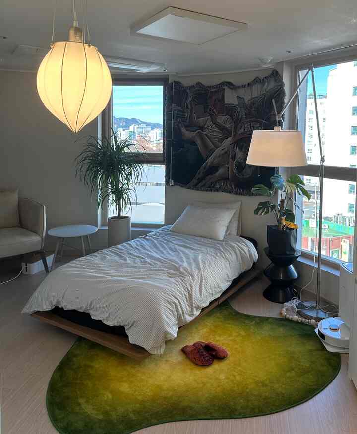 白を基調としたナチュラルモダンなワンルーム寝室、シングルベッドとグリーンのグラデーションラグが配置された落ち着いた空間