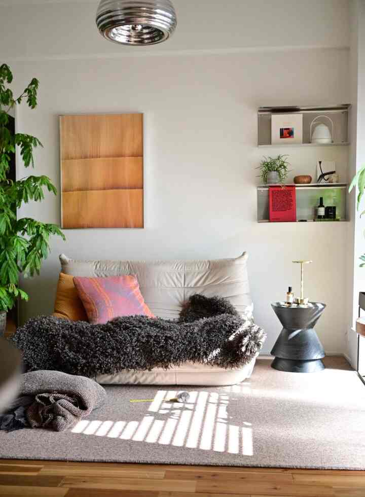 自然光が差し込む木製床のナチュラルモダンなリビング、中央にベージュのソファとスツールが配置されている