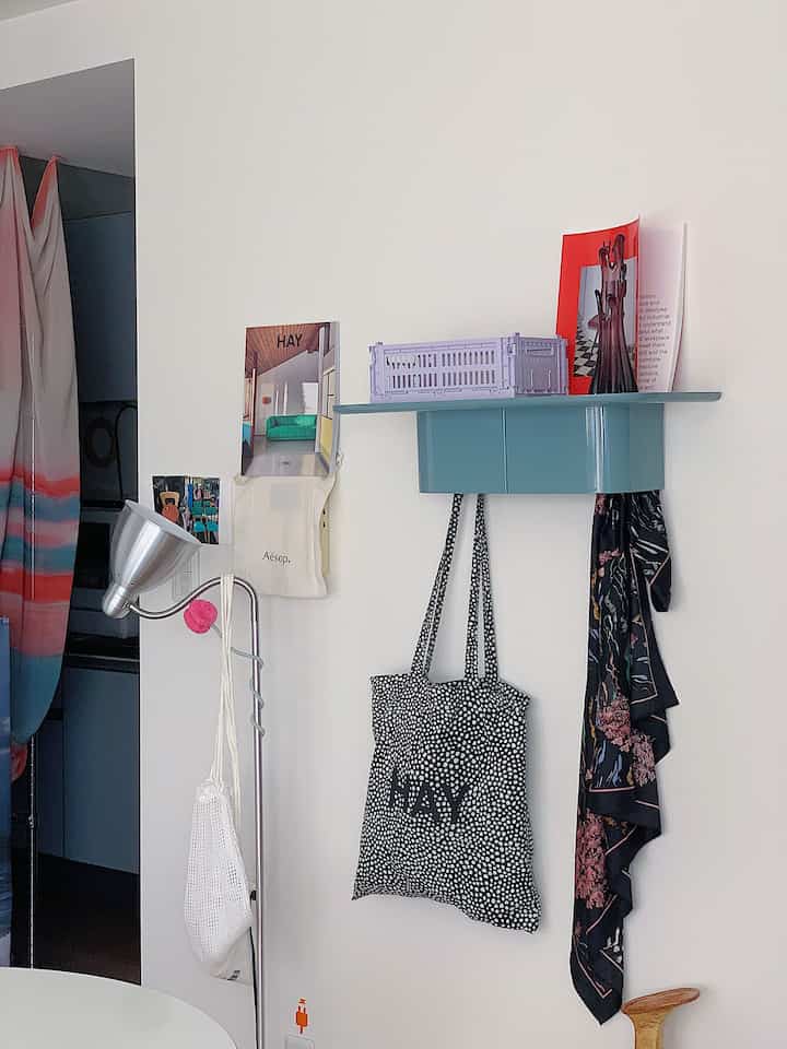 白い壁に緑色の壁掛け棚とフロアランプ、エコバッグが掛けられた清潔感のある1LDK北欧風インテリア