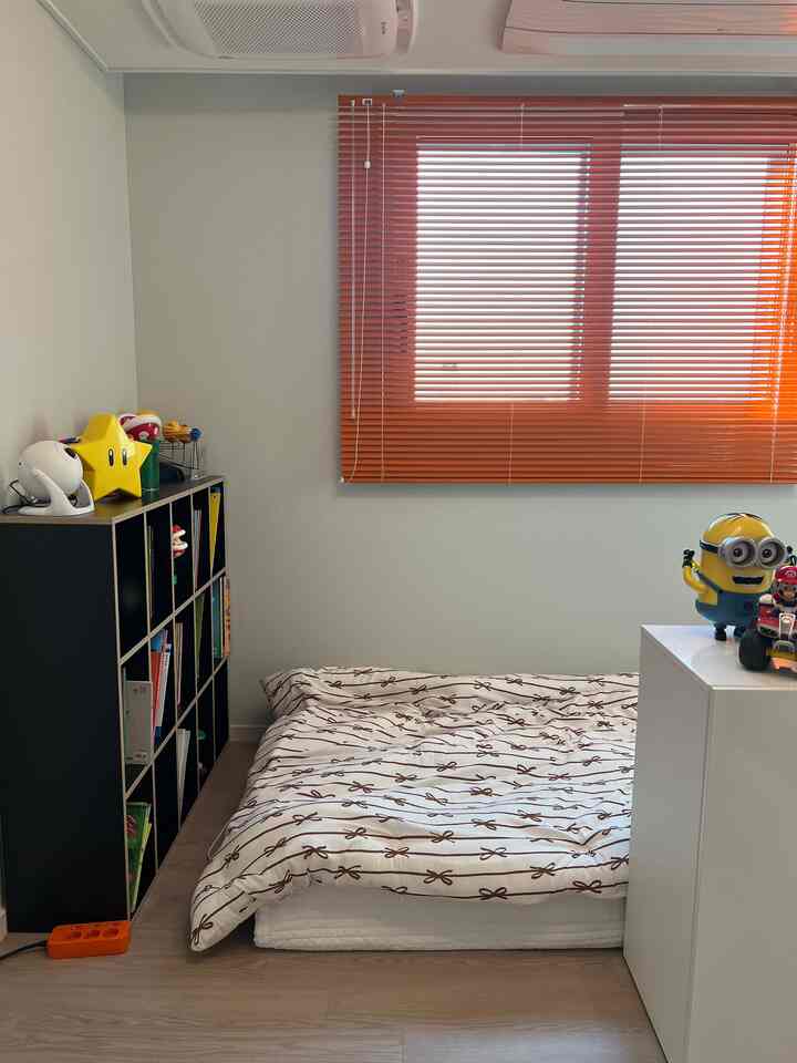 オレンジのブラインドと白い布団、黒い本棚が配置された子供部屋、自然な色調で暖かい雰囲気のあるインテリア