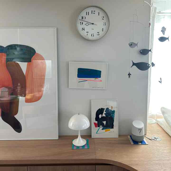 明るいグレーの壁と木製コンソールテーブルに、ミッドセンチュリーモダンのテーブルランプ、抽象画のポスター、魚のモビールが配置された居心地の良いリビング