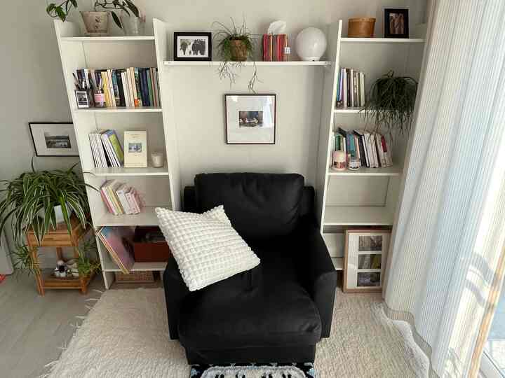白と黒のトーンの寝室コーナー、本棚とアームチェア、ラグ、植物が配置された雰囲気のある読書空間