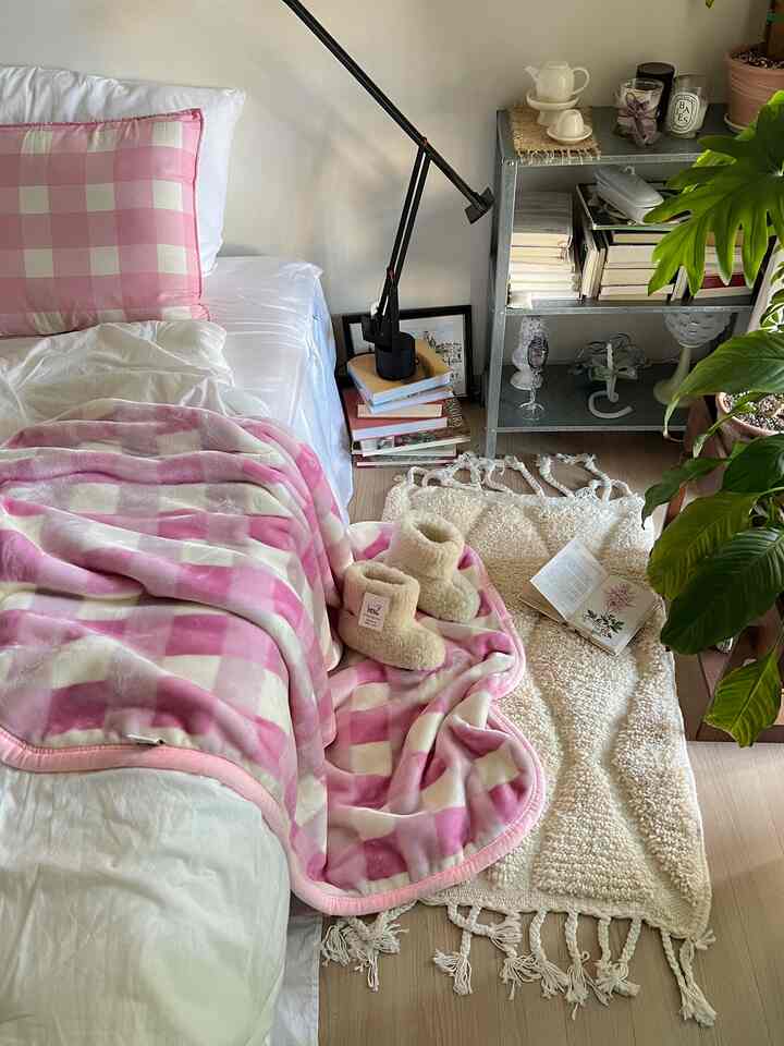 ピンクとアイボリーのトーンの寝室、ピンクのチェック柄寝具とアイボリーのラグが暖かく居心地の良い雰囲気を演出している