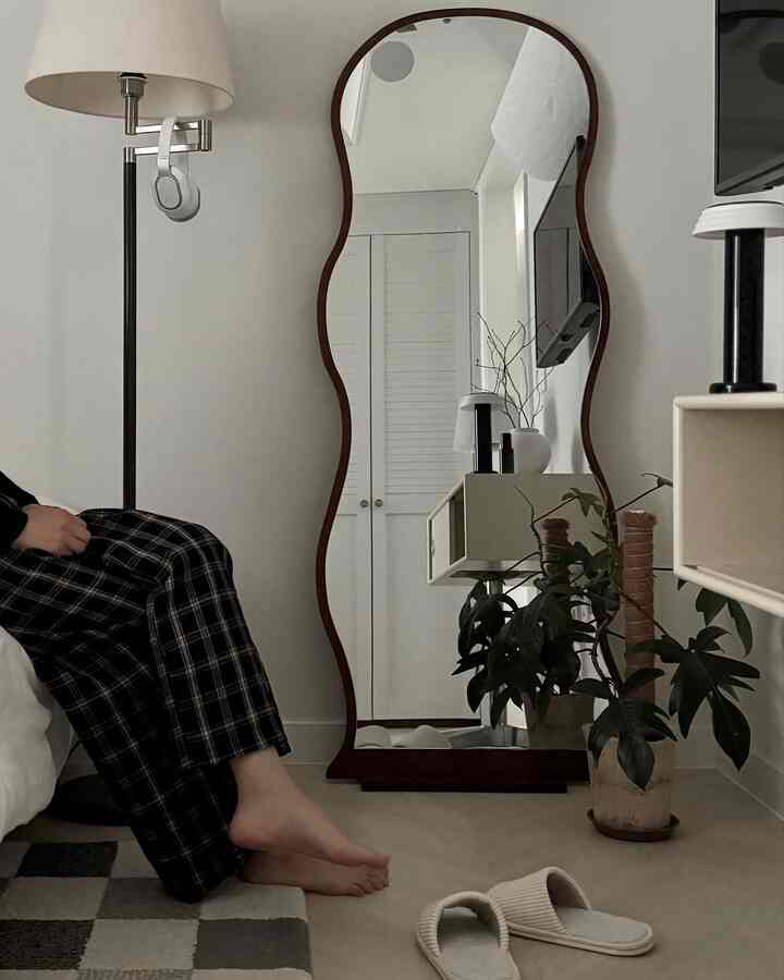 ナチュラルなベージュトーンのウォークインクローゼット、非対称の木製全身鏡とフロアランプ、植物が配された雰囲気のあるインテリア