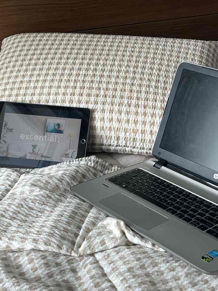 白とベージュのトーンの寝室、ノートパソコンとタブレットが置かれたコンパクトな空間