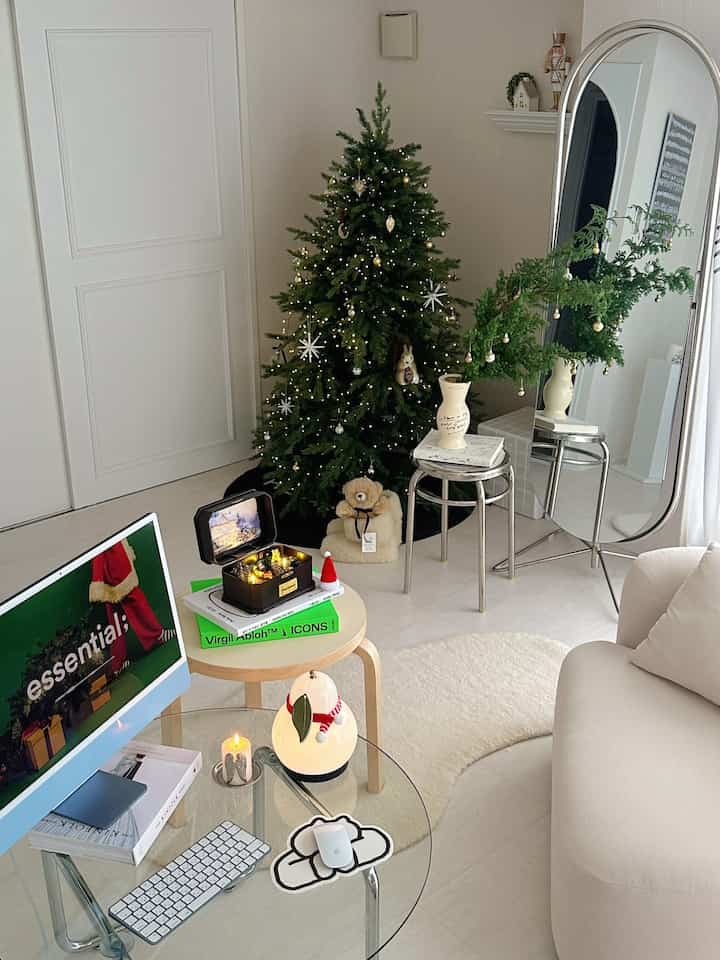 柔らかなホワイトとグリーンの色調のリビング、クリスマスツリーと鏡、スツールが配置された印象的で居心地の良いインテリア