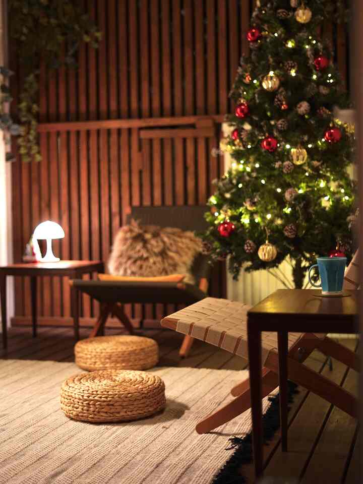 木目調の壁と床が印象的なリビングにクリスマスツリーと手作りのスツール、暖かい雰囲気のアームチェアが配置された居心地の良いホームパーティー空間