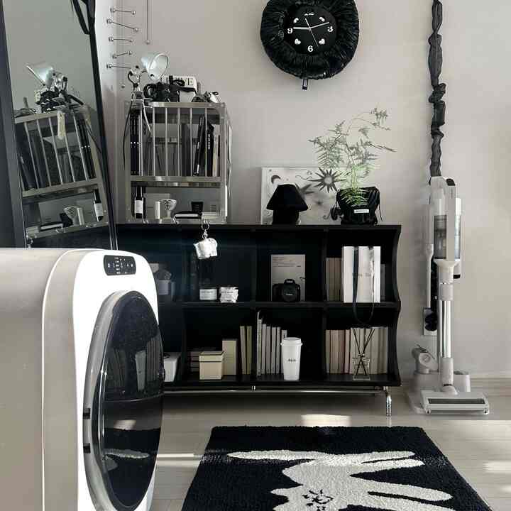 モダンな黒と白の色調の小さなリビング、整理された収納棚、ラグ、コードレス掃除機が配置された雰囲気のあるインテリア