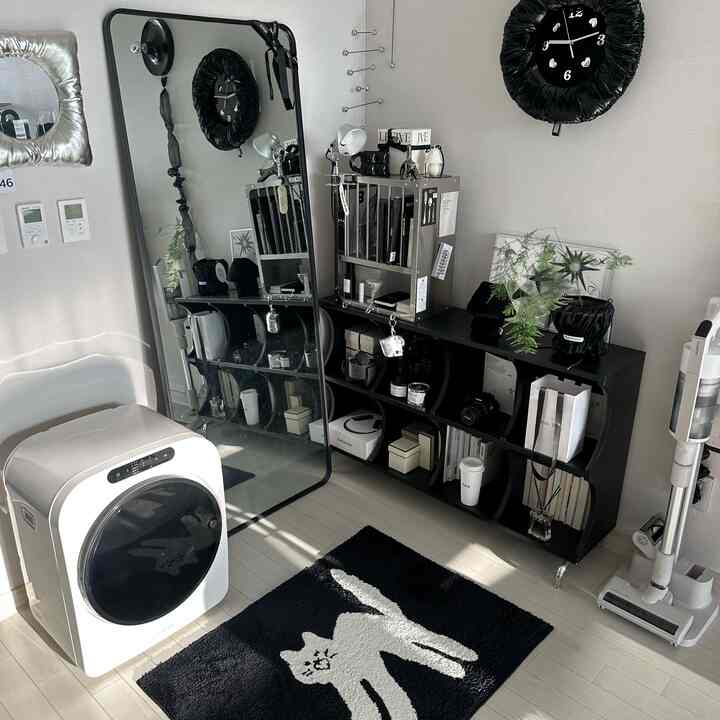 白い床と壁、黒い収納ラックと猫の柄のラグがある狭くてモダンなリビングスペース