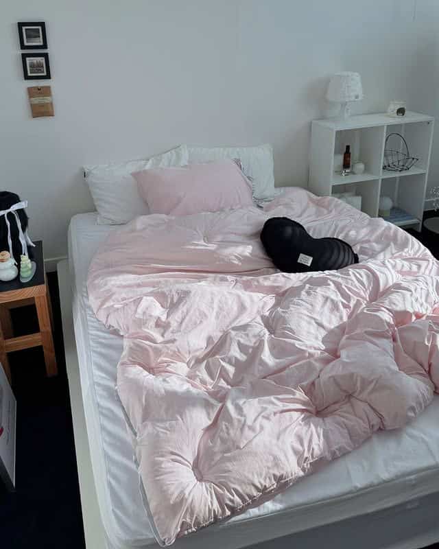 白とピンクの色調の寝室、シンプルなベッドとナイトテーブルが配置された落ち着いた空間