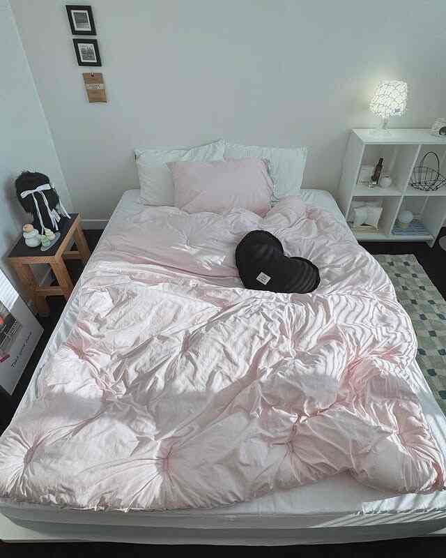 柔らかいピンクの寝具と白い壁が調和したモダンな寝室、リボン装飾の枕とサイドテーブルが配置された落ち着いた空間