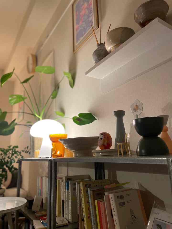 ナチュラルカラーの1Kワンルーム、壁掛け棚とテーブルランプ、植物が配置された落ち着いた空間