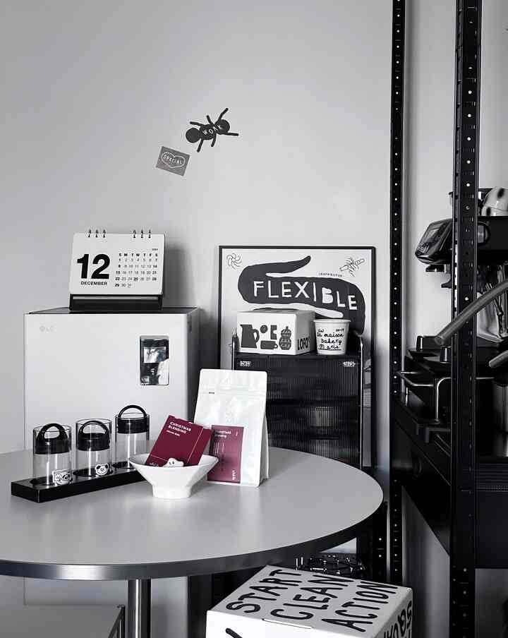 Modern studio apartment in white and black tones featuring a round table with coffee items and black metal shelving, creating a clean home cafe atmosphere