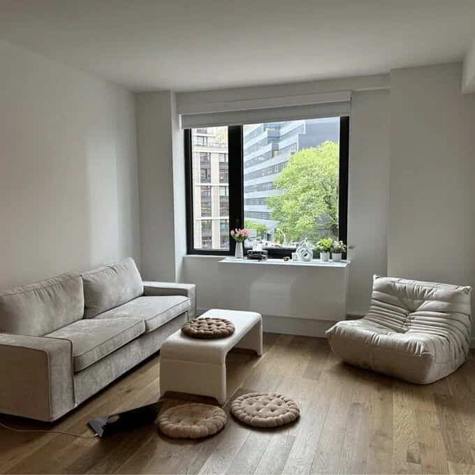 White-walled living room with wood tone flooring featuring a simple modern sofa and cozy armchair creating a comfortable space