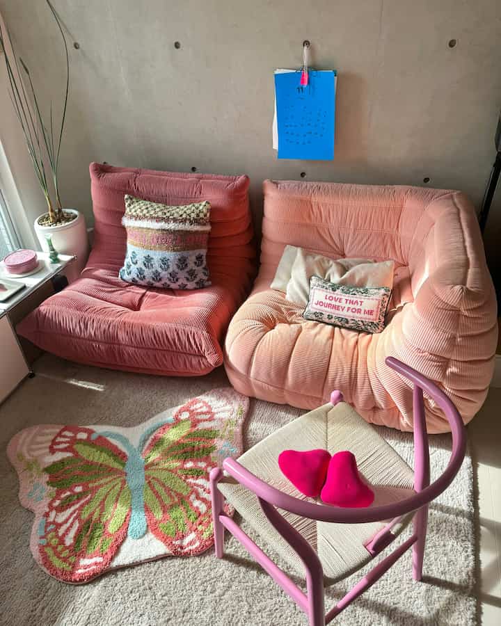 パステルピンクのソファと蝶の形のラグが配置された、自然光あふれる居心地の良いリビングスペース