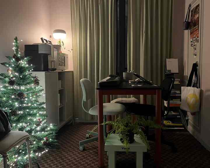 緑のカーテンと照明があるリビングスペース、クリスマスツリーとデスク、椅子が配置された温かみのあるホームオフィス環境