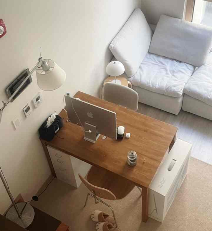 明るい白とナチュラルウッド調のリビング、コンピューターデスクとソファが配置されたモダンで居心地の良いホームオフィス空間