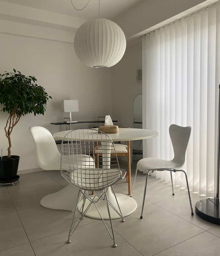 白とグレーの色調のダイニングルーム、丸テーブルとミッドセンチュリーモダンの椅子、大きなバブルペンダントライトが配置された印象的な空間