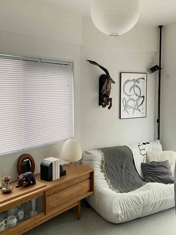 A white and light brown toned living room featuring an Akari lamp and sofa arranged in a cozy Japandi style space
