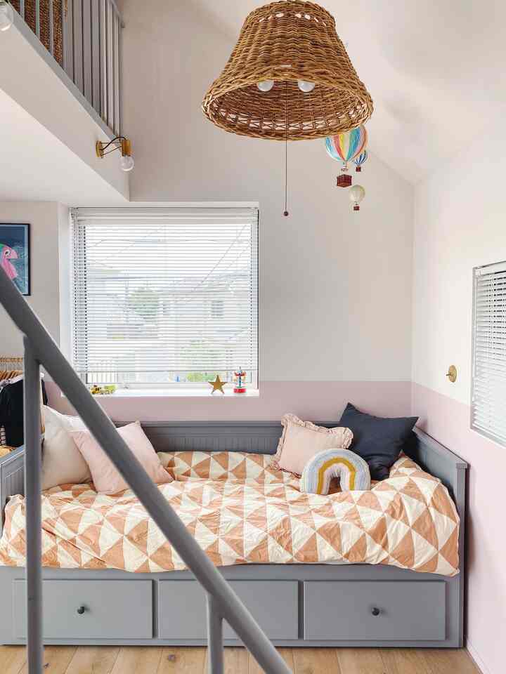 白とパステルピンクの子供部屋、グレーのデイベッドとウィッカーペンダントライトが配置された雰囲気のあるインテリア