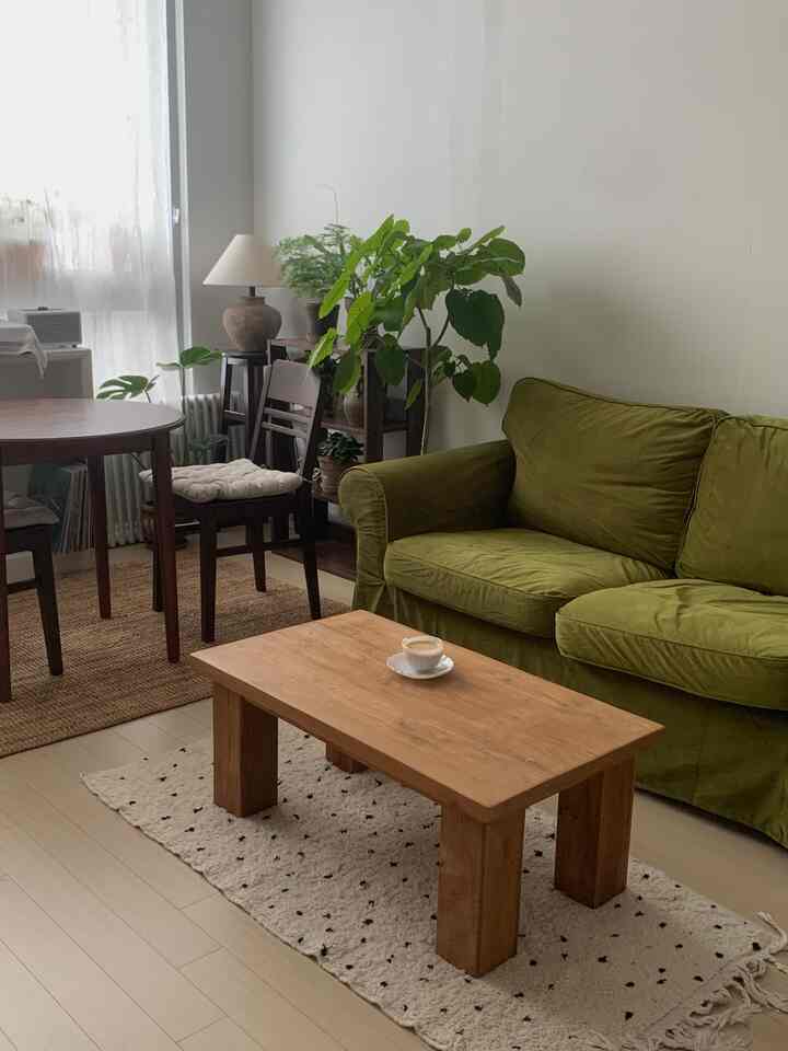 グリーンベルベットのソファと木製のコーヒーテーブルが配置されたナチュラルでヴィンテージ感のあるリビングルーム