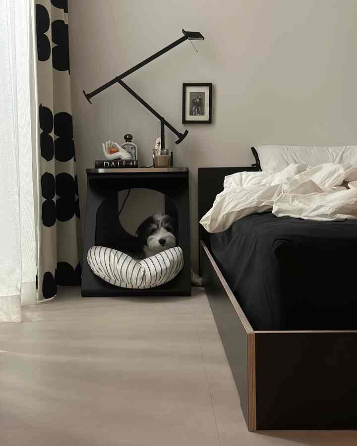 モノトーンの寝室、黒いベッドとナイトテーブルの上にテーブルランプがあり、中に犬のいるペットハウスが配置されたモダンなインテリア