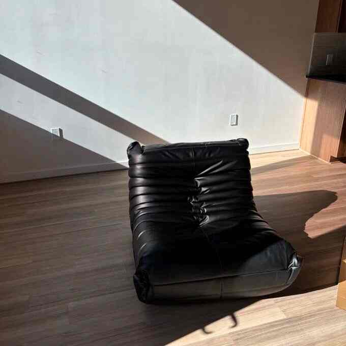 Modern, simple living space with wood-tone flooring and a black leather bean bag chair centered in the room