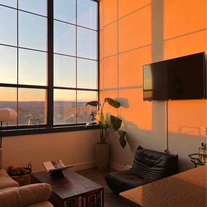 Warm beige and black toned living room featuring a large window with golden hour light, creating a minimal and modern atmosphere