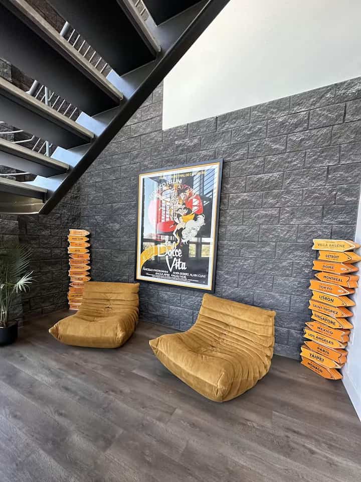 Modern industrial office lobby with gray stone wall and mustard armchairs arranged under metal staircase