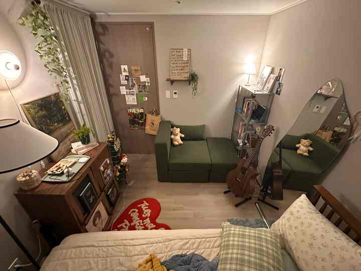 温かい照明と緑のソファがある小さなワンルームの寝室、ヴィンテージ家具と大きな鏡が配置された印象的な空間