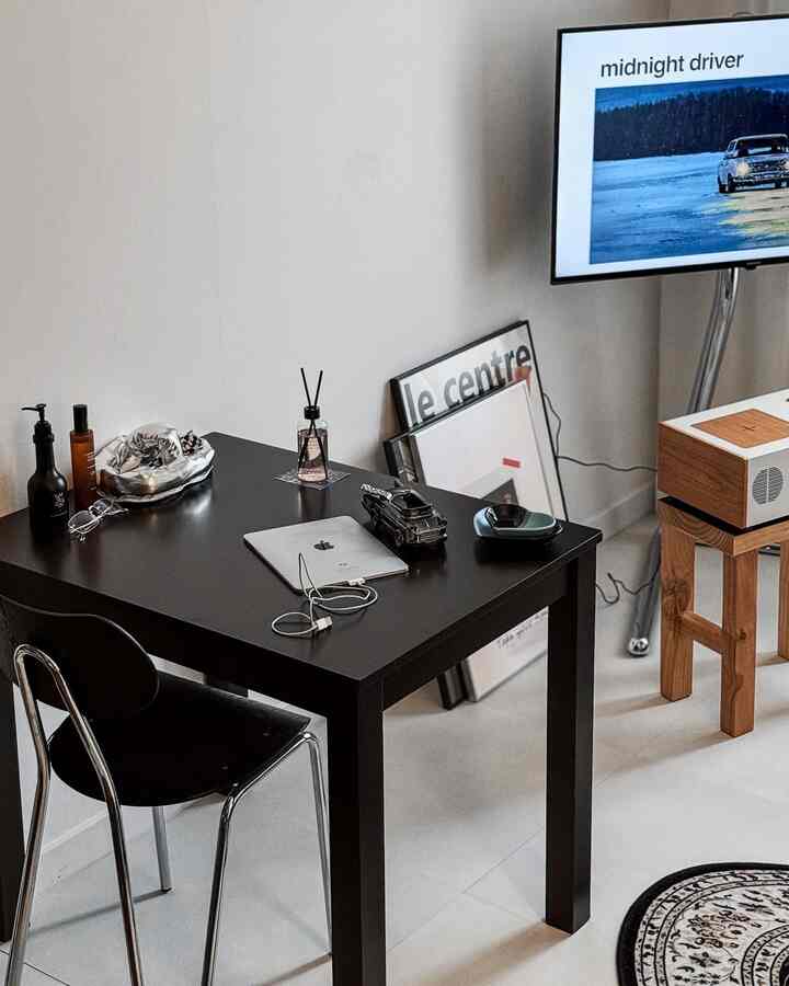 Minimal modern home office with white walls and floors, featuring a black desk and chair prominently center-left