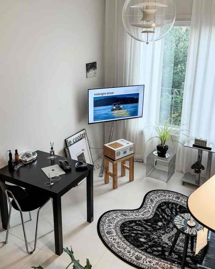 Modern two-person living room with white walls and floor, featuring black furniture and patterned rug