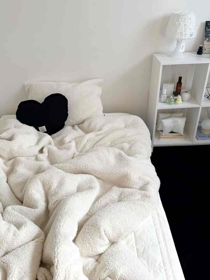 アイボリー調の寝室、ふわふわのシアリングマイクロファイバー寝具と黒いハートクッションが配置された、やわらかく暖かい雰囲気のあるインテリア
