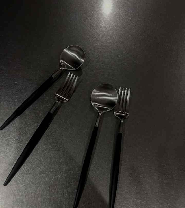 黒い持ち手のカトラリーセットが暗い金属の表面に整然と並べられたキッチン用品