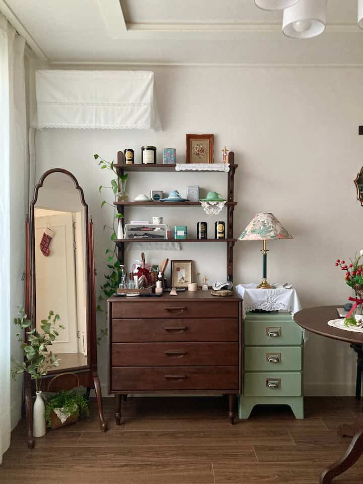 ナチュラルな木目調とヴィンテージ小物が調和したリビング、アンティーク家具とプランテリアが配置された落ち着いた雰囲気のインテリア