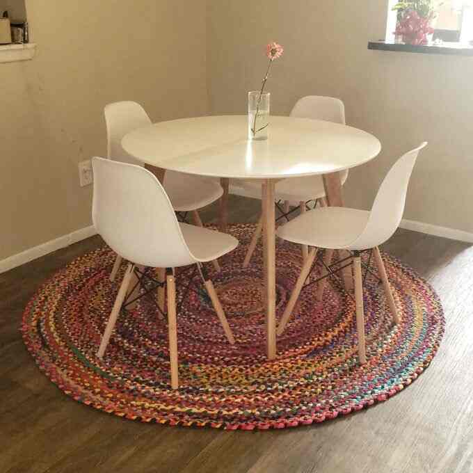 White and wood tone dining room featuring a round dining table and chairs on a colorful round braided carpet, creating a cozy vibe