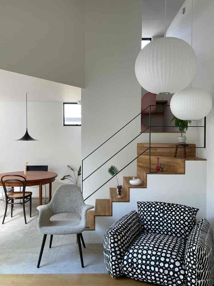 白と木目調のモダンなリビング、丸いペンダントライトと柄のソファが配置された落ち着いた雰囲気のインテリア