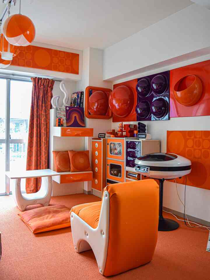 鮮やかなオレンジ色調のヴィンテージレトロなリビング空間、1970年代スタイルの家具と壁飾りが配置された印象的な部屋