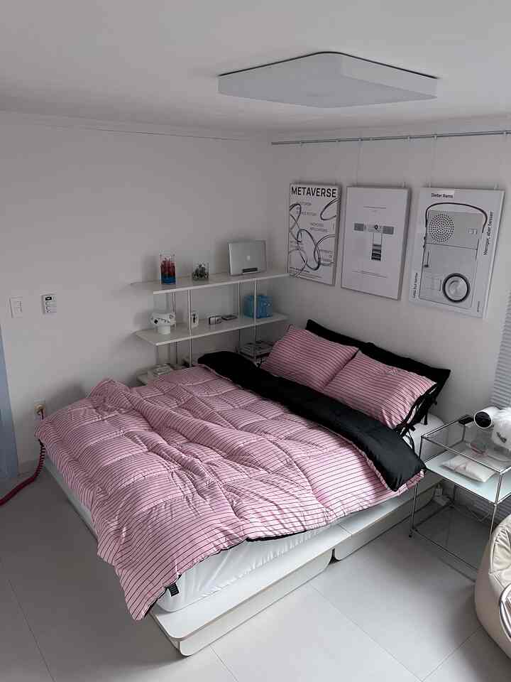 White and pink-black bedroom featuring striped bedding and mid-century modern posters, creating a modern atmosphere