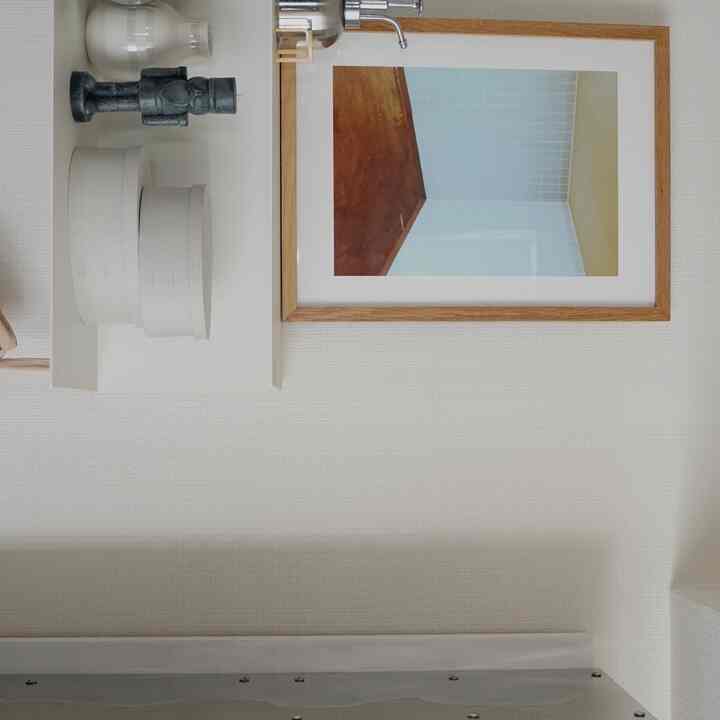 白とナチュラルトーンのキッチン壁、木製フレームのポスターと小さな白い棚が配置されたシンプルな空間