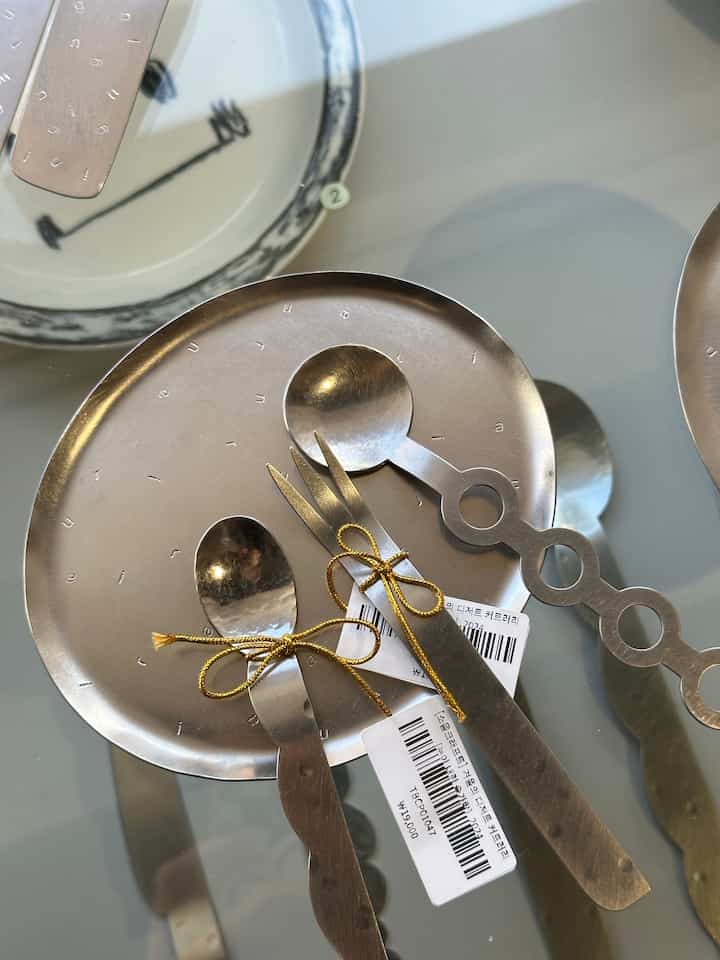 シルバー色の皿とカトラリーがガラステーブルに置かれたシンプルなキッチンアクセサリーの写真