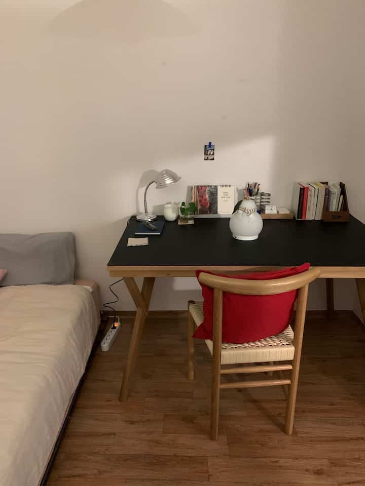 ブラウンの木目調床と黒い木製デスクが配置されたシンプルで落ち着いた寝室のインテリア