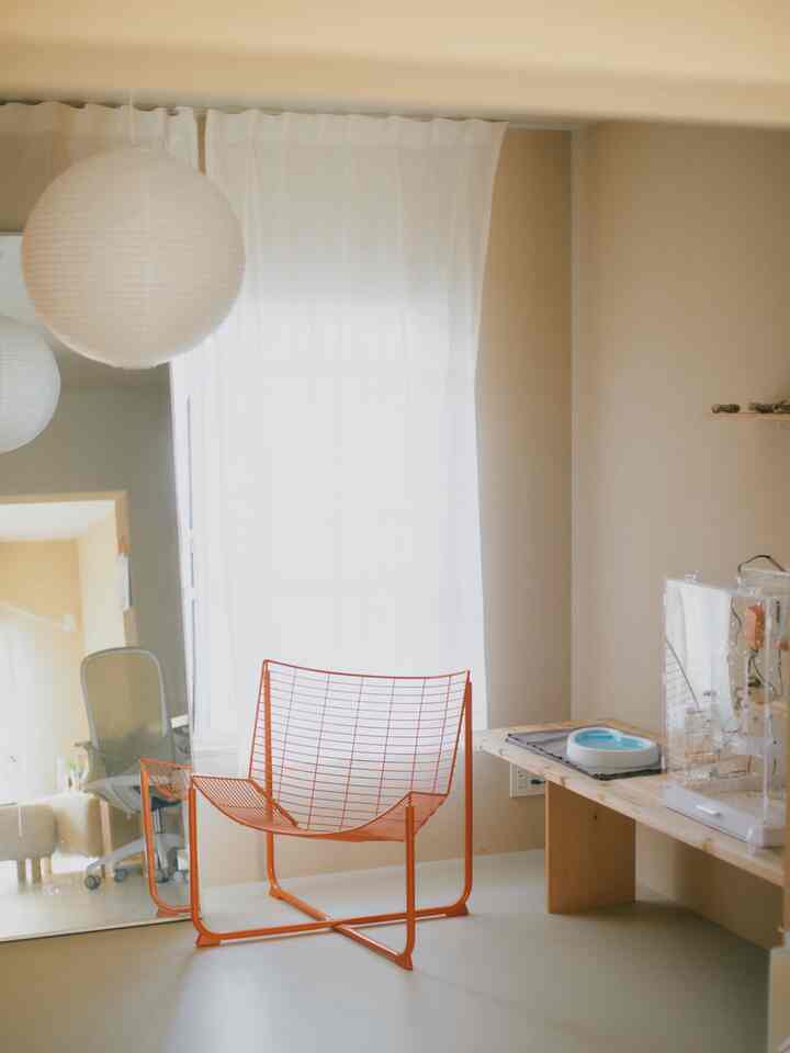 白とベージュのトーンの部屋にオレンジ色のワイヤーフレームチェアが配置されたシンプルで雰囲気のある読書スペース