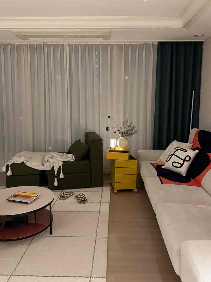 ベージュとグリーンの色調のリビング、モダンなソファとアームチェア、ラウンジ用ブランケットと黄色い収納が配置された雰囲気のある空間