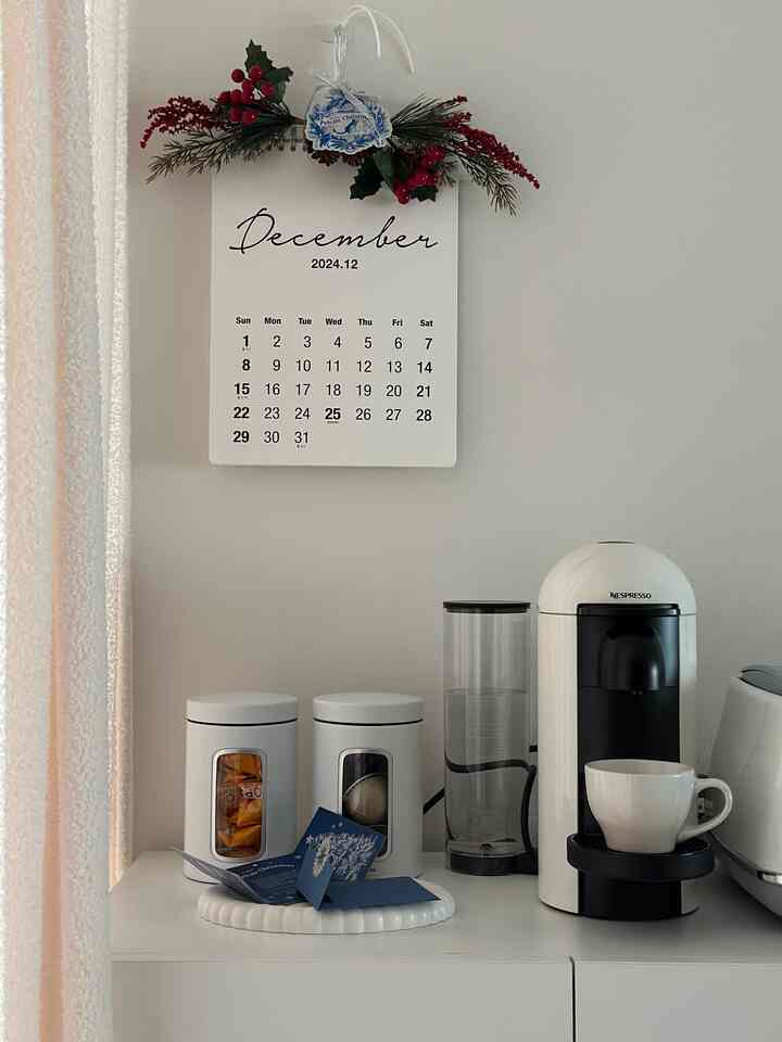 ホワイトトーンのミニおうちカフェ空間、ネスプレッソのコーヒーマシンと収納キャビネット、壁掛けカレンダーが配置された落ち着いた雰囲気のインテリア