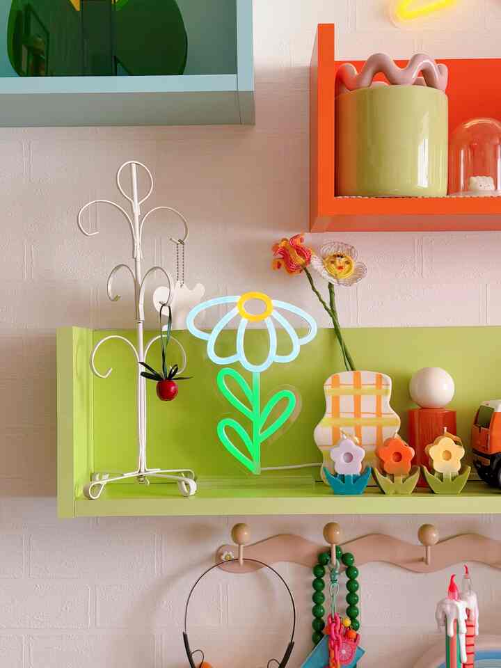 A pastel-toned wall with a bright green shelf featuring a cute flower-shaped neon light and various colorful decor items in a charming interior space