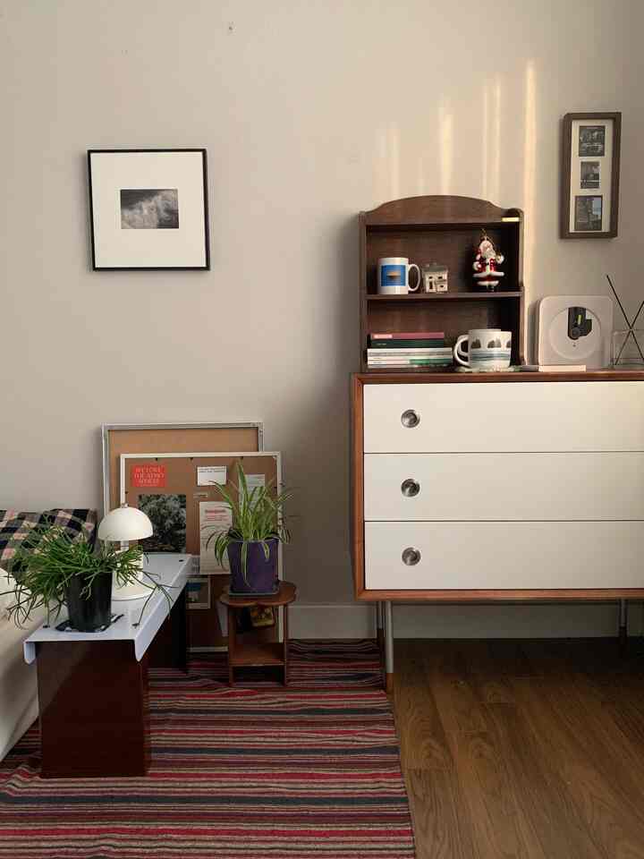 ウッドトーンとホワイト調の寝室、ナイトテーブルと棚に植物や小物が配置された雰囲気あるコンパクトな空間